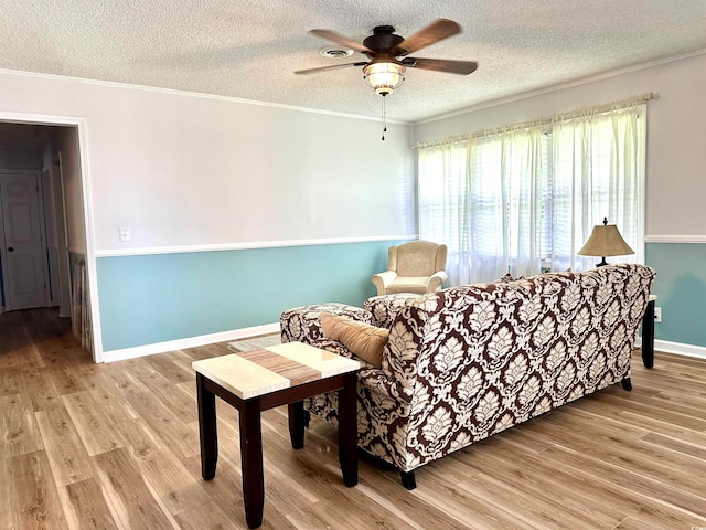 living room with ceiling fan, a textured ceiling, light hardwood / wood-style flooring, and crown molding