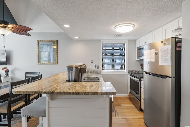 kitchen featuring a textured ceiling, light hardwood / wood-style flooring, white cabinetry, stainless steel appliances, and a breakfast bar