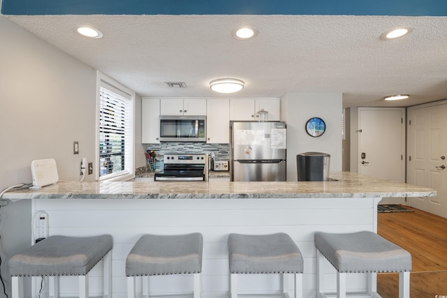 kitchen with white cabinets, a textured ceiling, light hardwood / wood-style flooring, stainless steel appliances, and a breakfast bar area