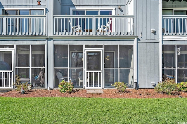 back of house featuring a balcony, a sunroom, and a lawn