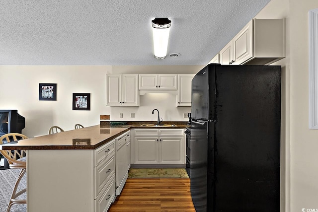 kitchen with dark hardwood / wood-style floors, kitchen peninsula, sink, a breakfast bar area, and black refrigerator