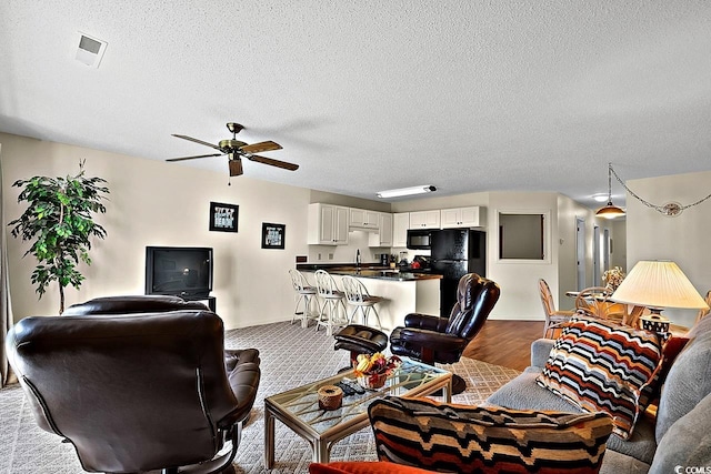 living room featuring a textured ceiling, carpet flooring, ceiling fan, and sink