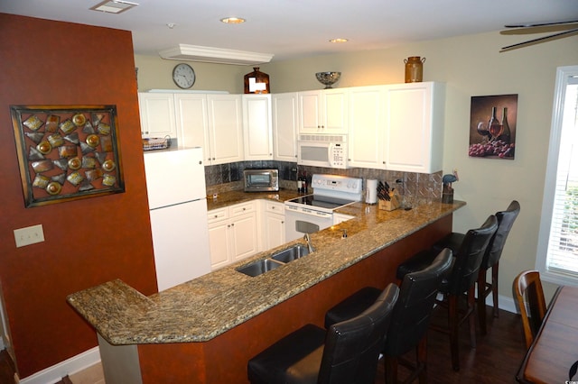 kitchen featuring decorative backsplash, white appliances, white cabinets, and a kitchen bar