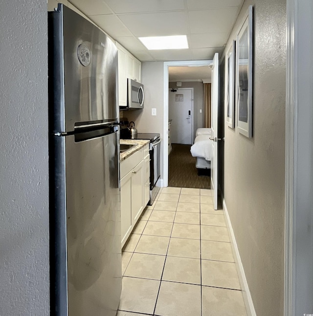 kitchen featuring a drop ceiling, white cabinets, appliances with stainless steel finishes, and light tile patterned floors