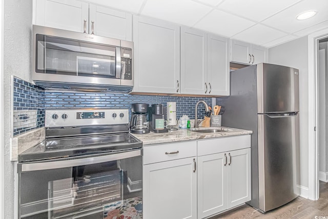 kitchen with tasteful backsplash, white cabinetry, appliances with stainless steel finishes, light hardwood / wood-style floors, and sink