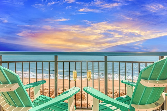 balcony at dusk featuring a beach view and a water view