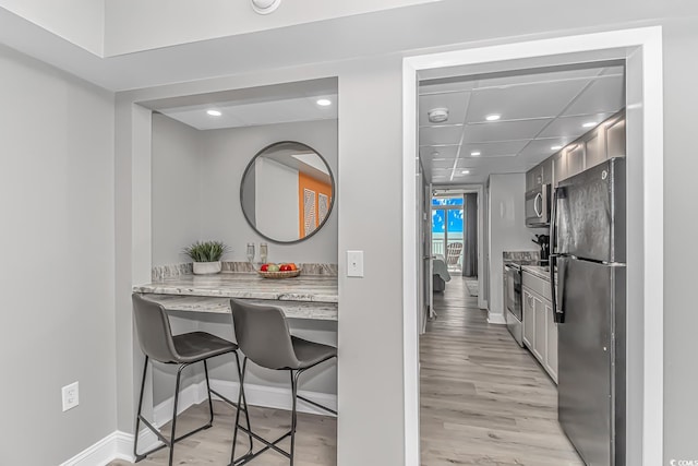 kitchen with light stone counters, a breakfast bar area, appliances with stainless steel finishes, and light wood-type flooring