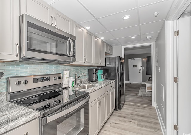 kitchen with sink, tasteful backsplash, appliances with stainless steel finishes, light stone countertops, and light hardwood / wood-style floors