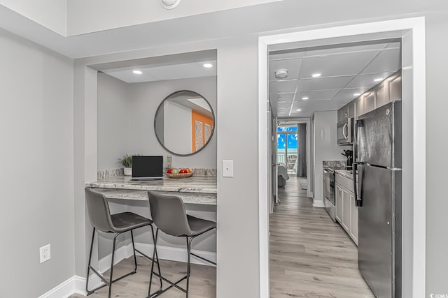 kitchen featuring a kitchen bar, light hardwood / wood-style floors, appliances with stainless steel finishes, and light stone counters