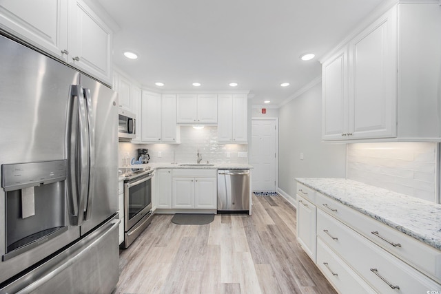 kitchen with light wood-style flooring, stainless steel appliances, a sink, white cabinets, and light stone countertops