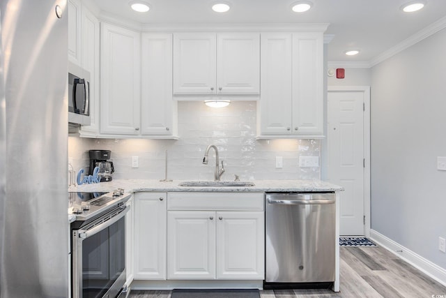 kitchen with ornamental molding, light stone countertops, stainless steel appliances, white cabinetry, and a sink