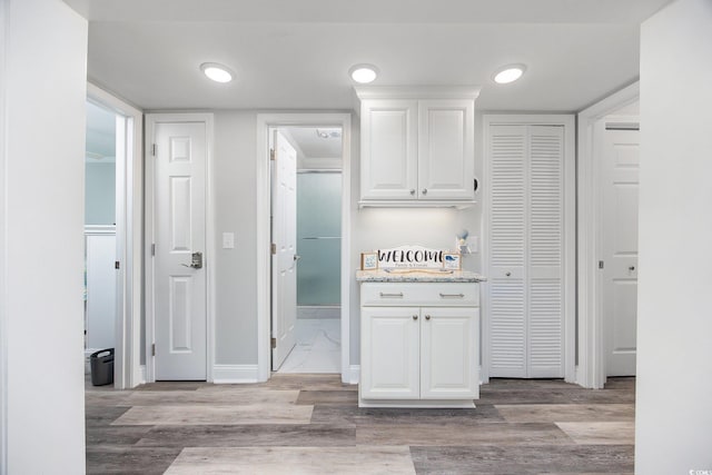 kitchen featuring light wood-type flooring, light stone countertops, white cabinetry, and baseboards