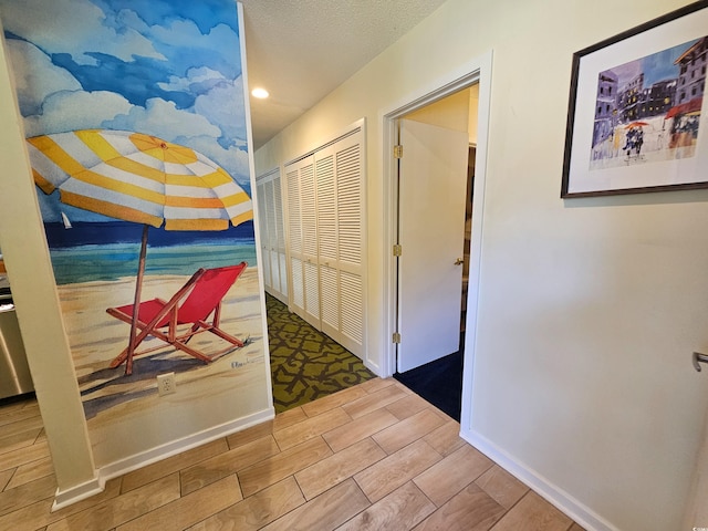 hall with baseboards, a textured ceiling, and wood finish floors