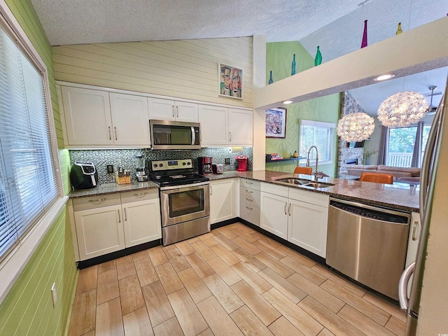 kitchen with a peninsula, appliances with stainless steel finishes, a sink, and white cabinetry