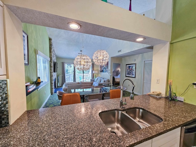 kitchen featuring stainless steel dishwasher, a chandelier, sink, dark stone countertops, and a textured ceiling