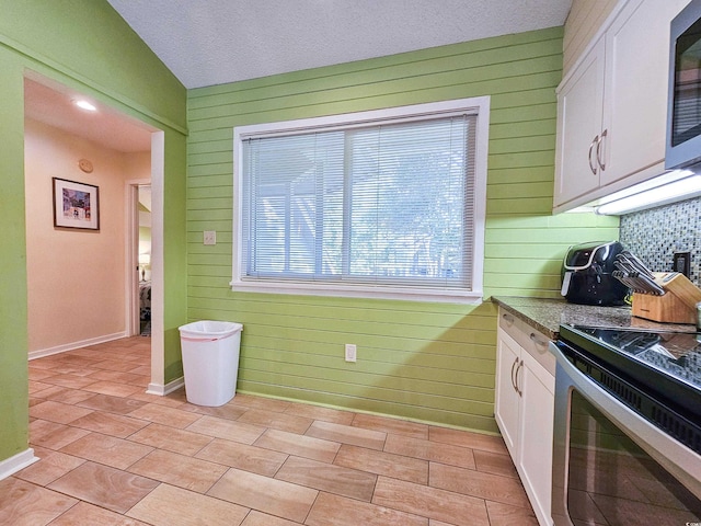 kitchen with light tile patterned flooring, wooden walls, and white cabinetry