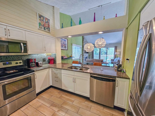 kitchen with appliances with stainless steel finishes, dark stone countertops, decorative light fixtures, white cabinetry, and a sink