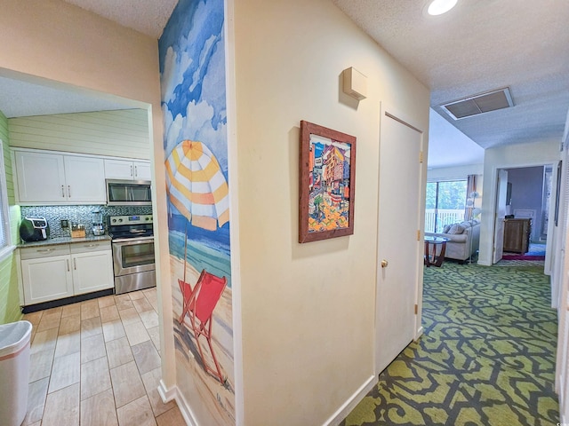 corridor with light colored carpet and a textured ceiling