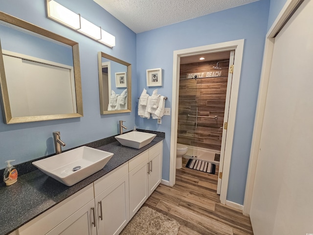 bathroom featuring toilet, vanity, wood-type flooring, tiled shower, and a textured ceiling