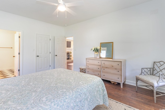 bedroom featuring ceiling fan, a fireplace, dark wood-style flooring, and baseboards