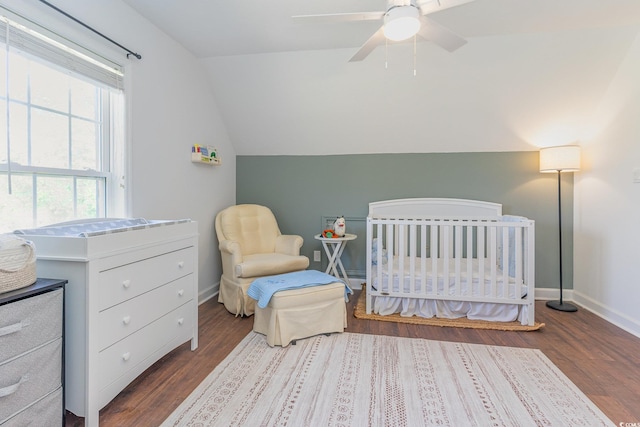 bedroom with a crib, a ceiling fan, wood finished floors, baseboards, and vaulted ceiling