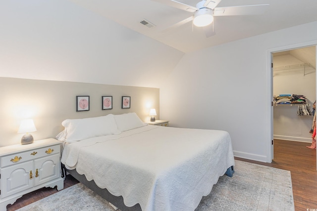 bedroom featuring baseboards, visible vents, dark wood-style flooring, vaulted ceiling, and a spacious closet