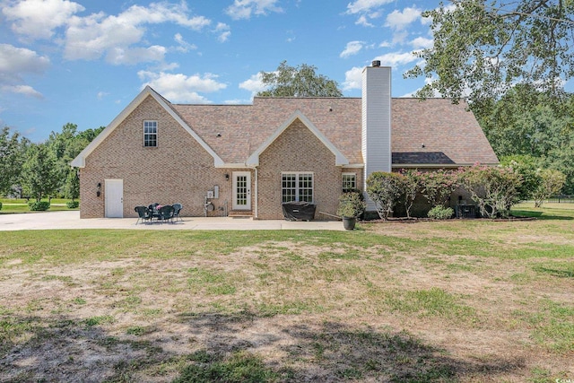 back of property featuring a patio, a yard, brick siding, and a chimney