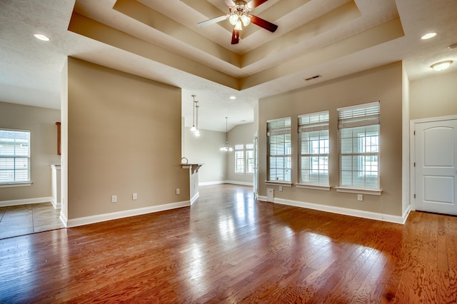 unfurnished living room with hardwood / wood-style floors, ceiling fan with notable chandelier, and a raised ceiling