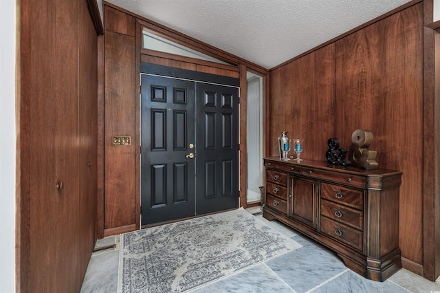 foyer entrance featuring vaulted ceiling, a textured ceiling, and wood walls