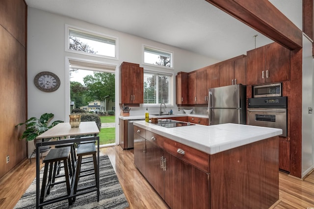 kitchen with stainless steel appliances, a towering ceiling, light hardwood / wood-style floors, and a kitchen island