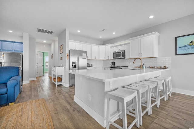 kitchen featuring wood-type flooring, a breakfast bar, kitchen peninsula, appliances with stainless steel finishes, and white cabinetry