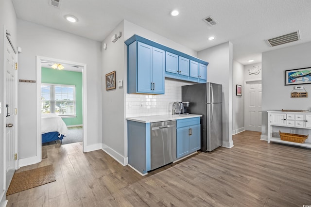 kitchen featuring light wood-type flooring, backsplash, stainless steel appliances, blue cabinetry, and a textured ceiling