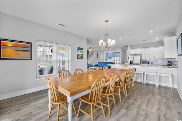 dining room featuring ceiling fan with notable chandelier and light hardwood / wood-style floors