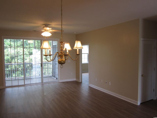 spare room with ceiling fan with notable chandelier, a wealth of natural light, and dark hardwood / wood-style floors