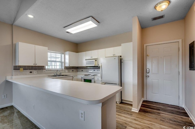 kitchen featuring light countertops, white appliances, a peninsula, and white cabinetry