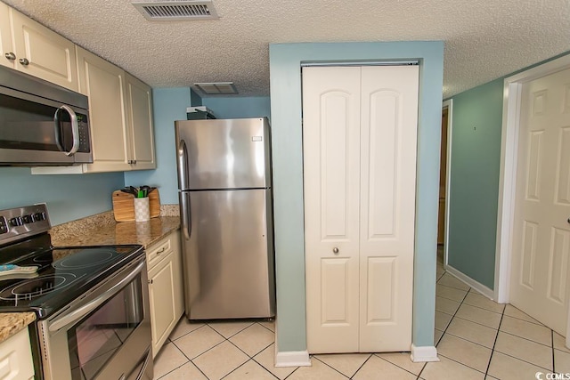 kitchen with appliances with stainless steel finishes, light tile patterned floors, light stone counters, and a textured ceiling