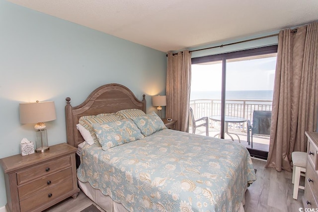 bedroom with light wood-style floors, a water view, and access to exterior