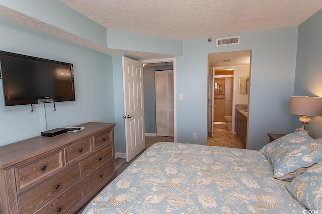 bedroom featuring ensuite bath, a textured ceiling, light tile patterned floors, and a closet