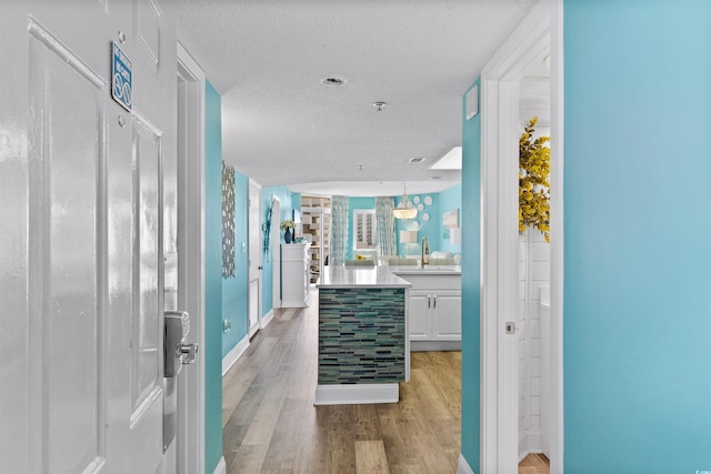 interior space with a textured ceiling, sink, and light hardwood / wood-style flooring