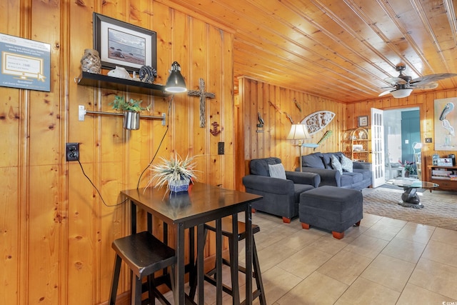 living room with wood ceiling, light tile patterned flooring, wood walls, and ceiling fan