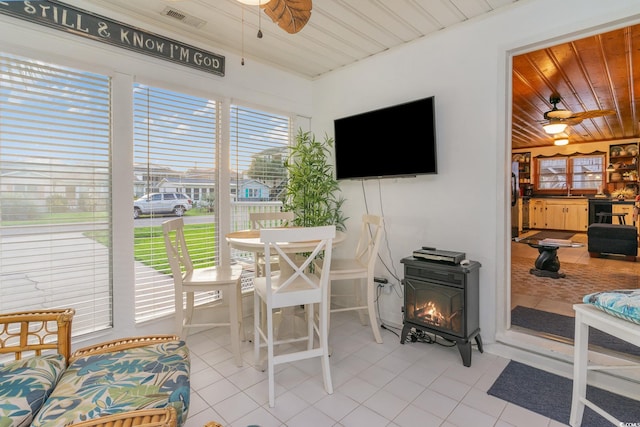 sunroom featuring a wood stove, plenty of natural light, ceiling fan, and wooden ceiling