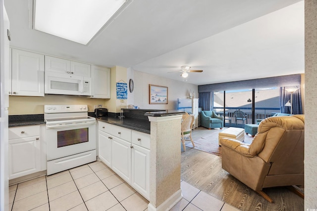 kitchen with dark countertops, open floor plan, a peninsula, white cabinets, and white appliances