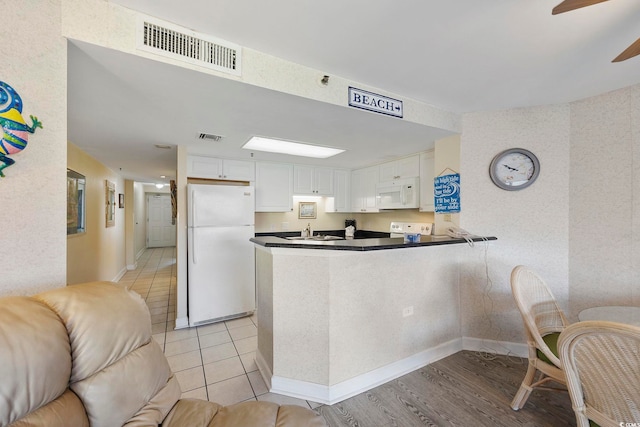 kitchen featuring visible vents, a peninsula, white appliances, white cabinetry, and a sink