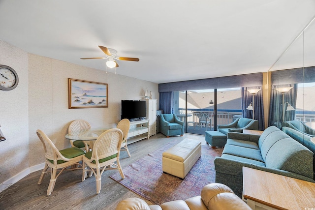 living room with ceiling fan, a wall of windows, baseboards, and wood finished floors