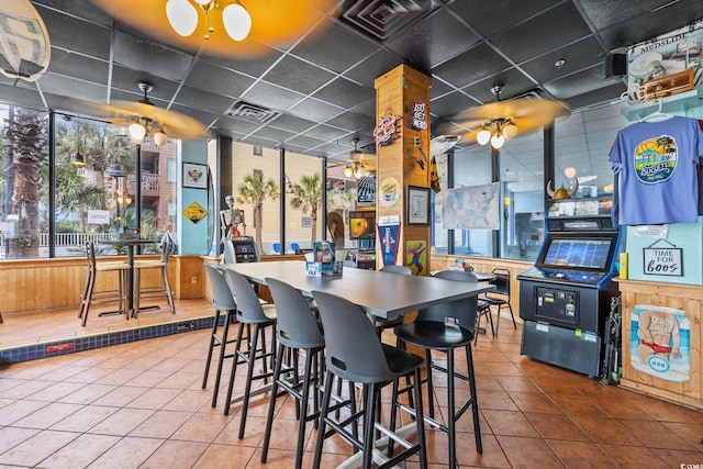 dining space with ceiling fan, a drop ceiling, and tile patterned floors