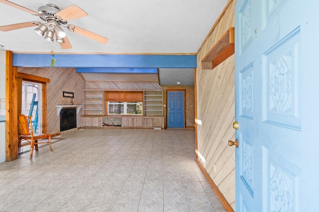 unfurnished living room with beam ceiling, wooden walls, and ceiling fan