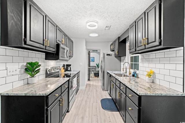 kitchen with sink, a textured ceiling, light hardwood / wood-style flooring, stainless steel appliances, and light stone countertops