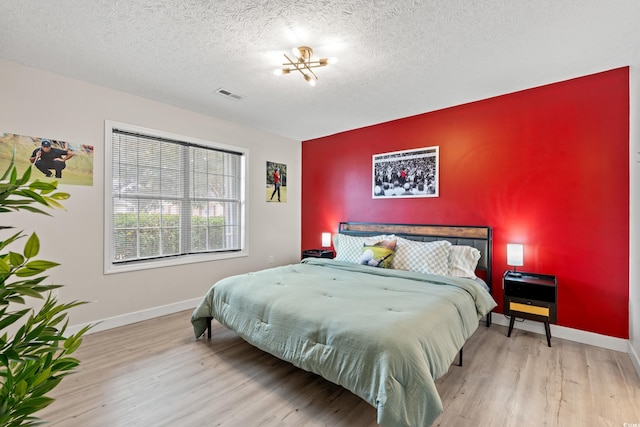 bedroom featuring light wood-type flooring, a textured ceiling, and a notable chandelier