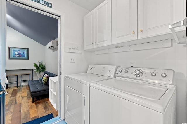 clothes washing area with cabinets, hardwood / wood-style floors, washing machine and dryer, and a wall unit AC