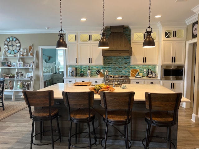 kitchen with a kitchen island with sink, custom exhaust hood, and hardwood / wood-style flooring